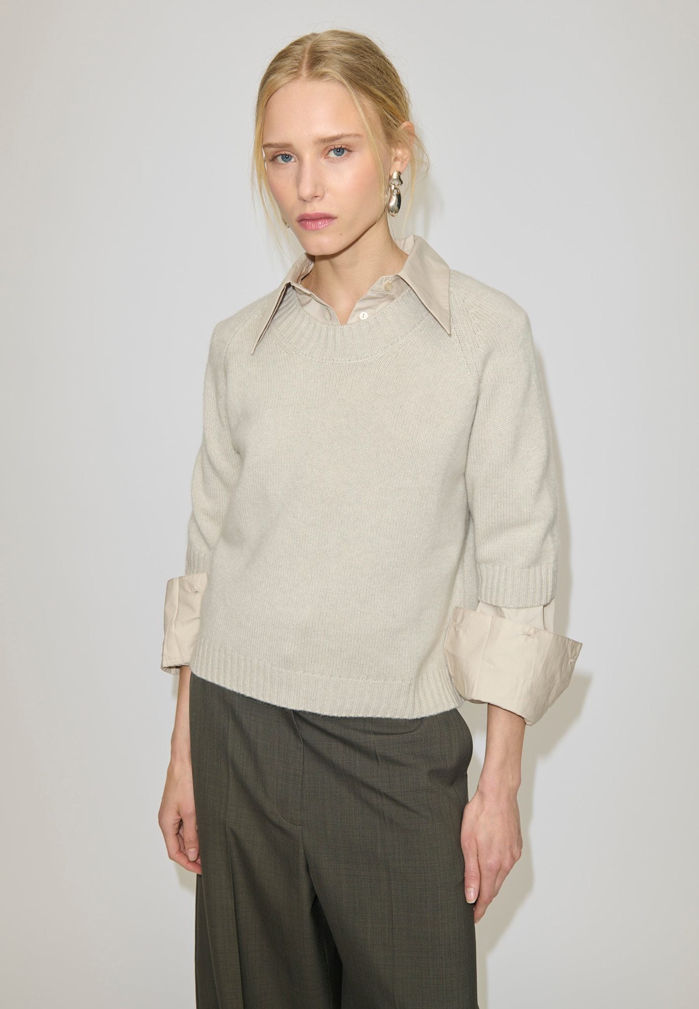 A person wears a beige Herskind ApS Josie Cashmere Knit Blouse layered over a collared shirt with cuffs visible at the sleeves.