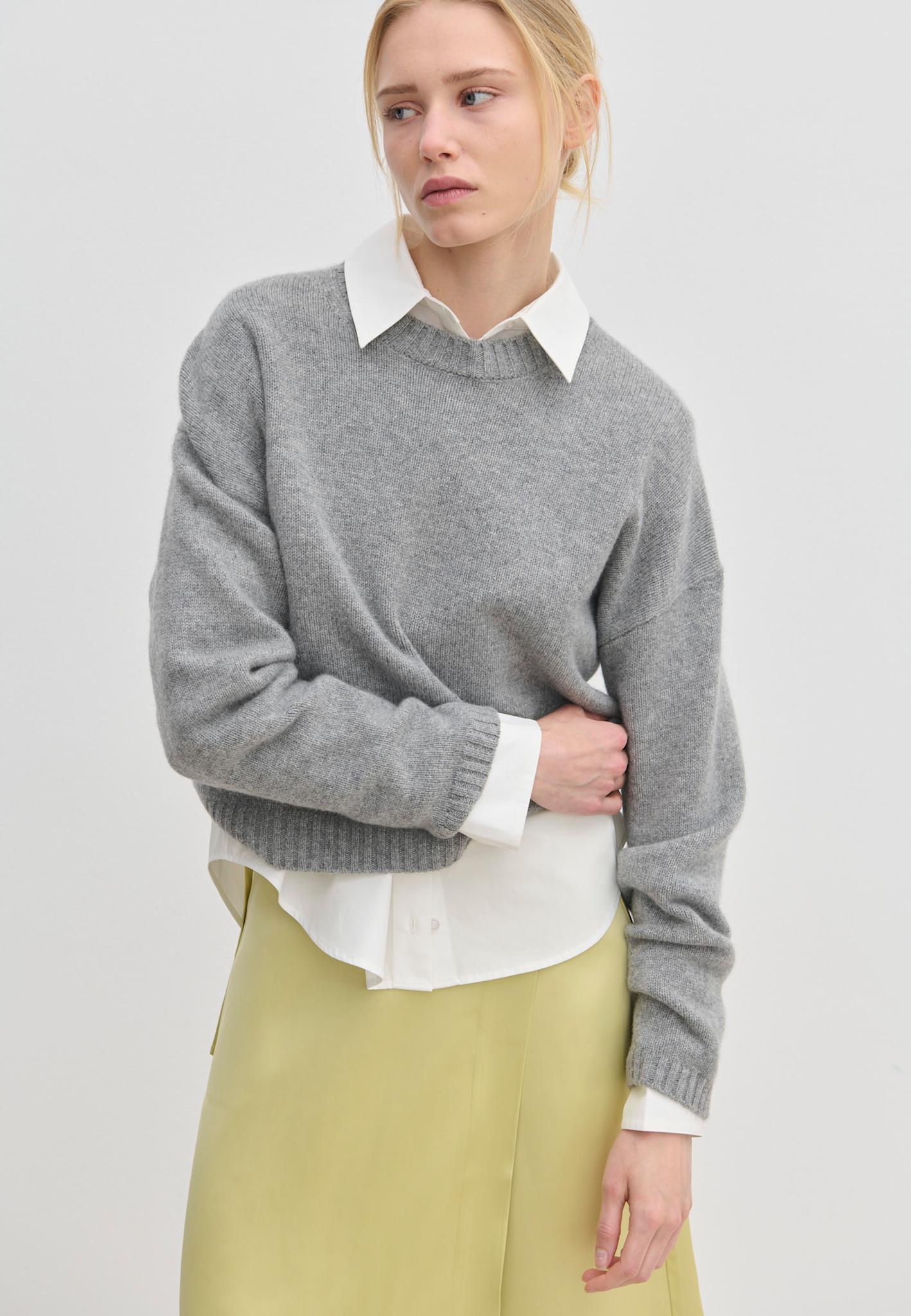 A model wears a grey Constantine Cashmere Knit Blouse by Herskind ApS over a white collared shirt and a pale yellow skirt.