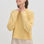 A person wearing a yellow Constantine Cashmere Knit Blouse featuring a crew-neck, long sleeves, and a ribbed hem.