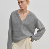 A person wearing a grey V-neck Micky Cashmere Knit Blouse by Herskind ApS and a cream wrap skirt.