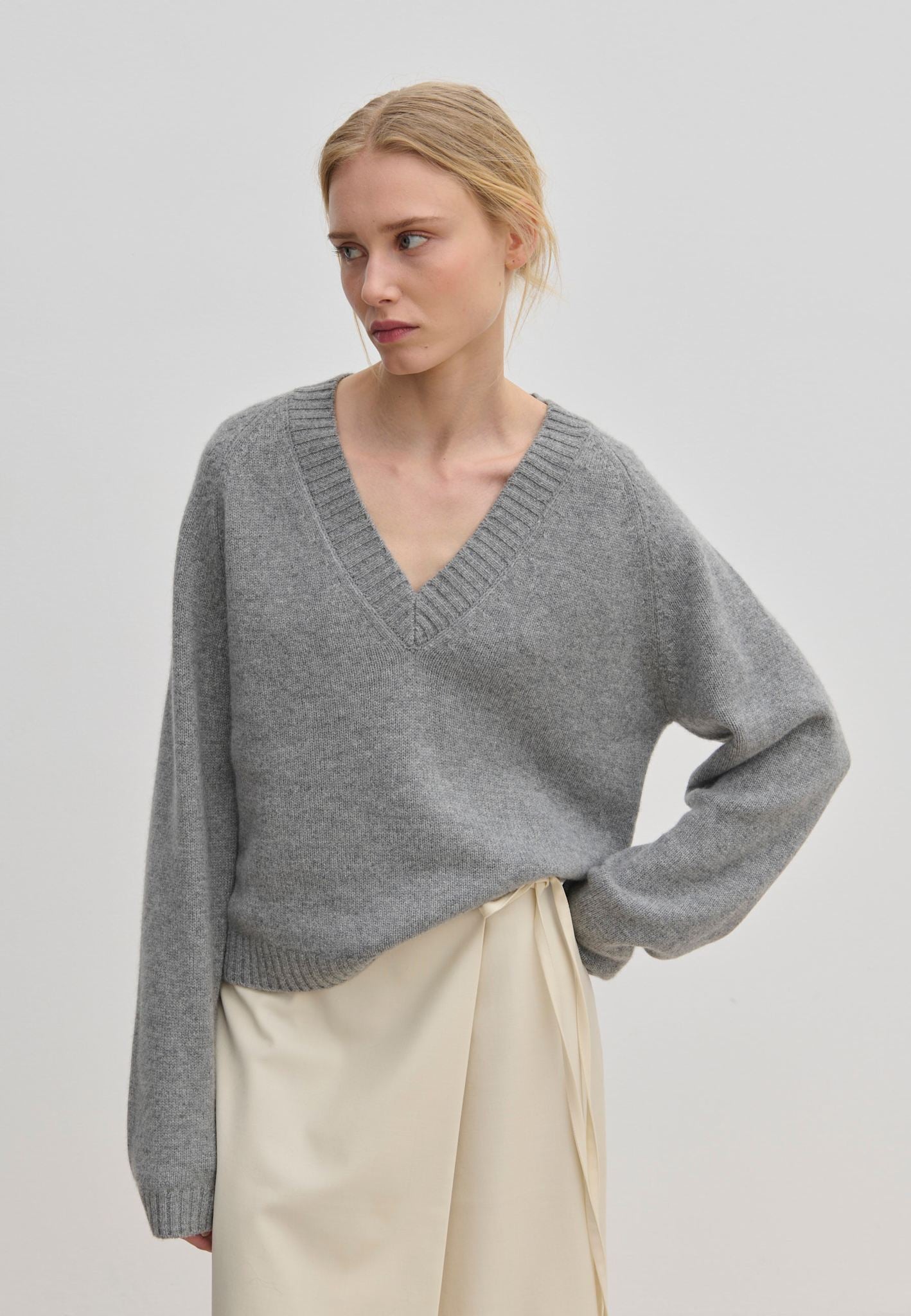 A person wearing a grey V-neck Micky Cashmere Knit Blouse by Herskind ApS and a cream wrap skirt.