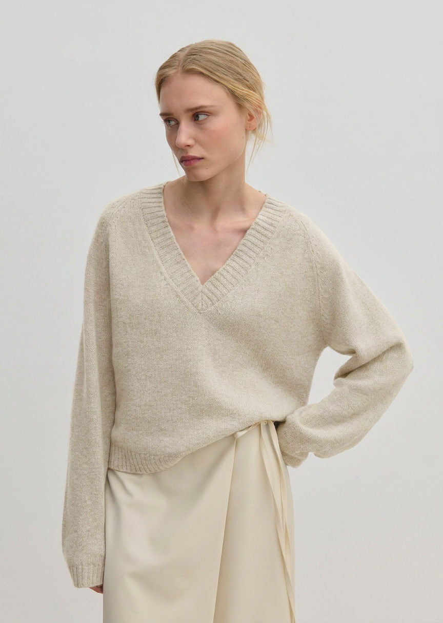 A person wearing a relaxed fit, v-neck Micky Cashmere Knit Blouse by Herskind ApS over a light-colored wrap skirt.