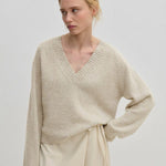 A person wearing a relaxed fit, v-neck Micky Cashmere Knit Blouse by Herskind ApS over a light-colored wrap skirt.