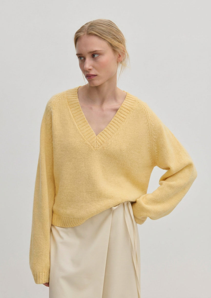 A person wearing a relaxed fit, pale yellow V-neck Micky Cashmere Knit Blouse by Herskind ApS.