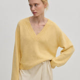 A person wearing a relaxed fit, pale yellow V-neck Micky Cashmere Knit Blouse by Herskind ApS.