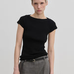 A person wearing a black, short-sleeved Erica Knit T-shirt by Herskind ApS, paired with grey patterned trousers and a thin belt.