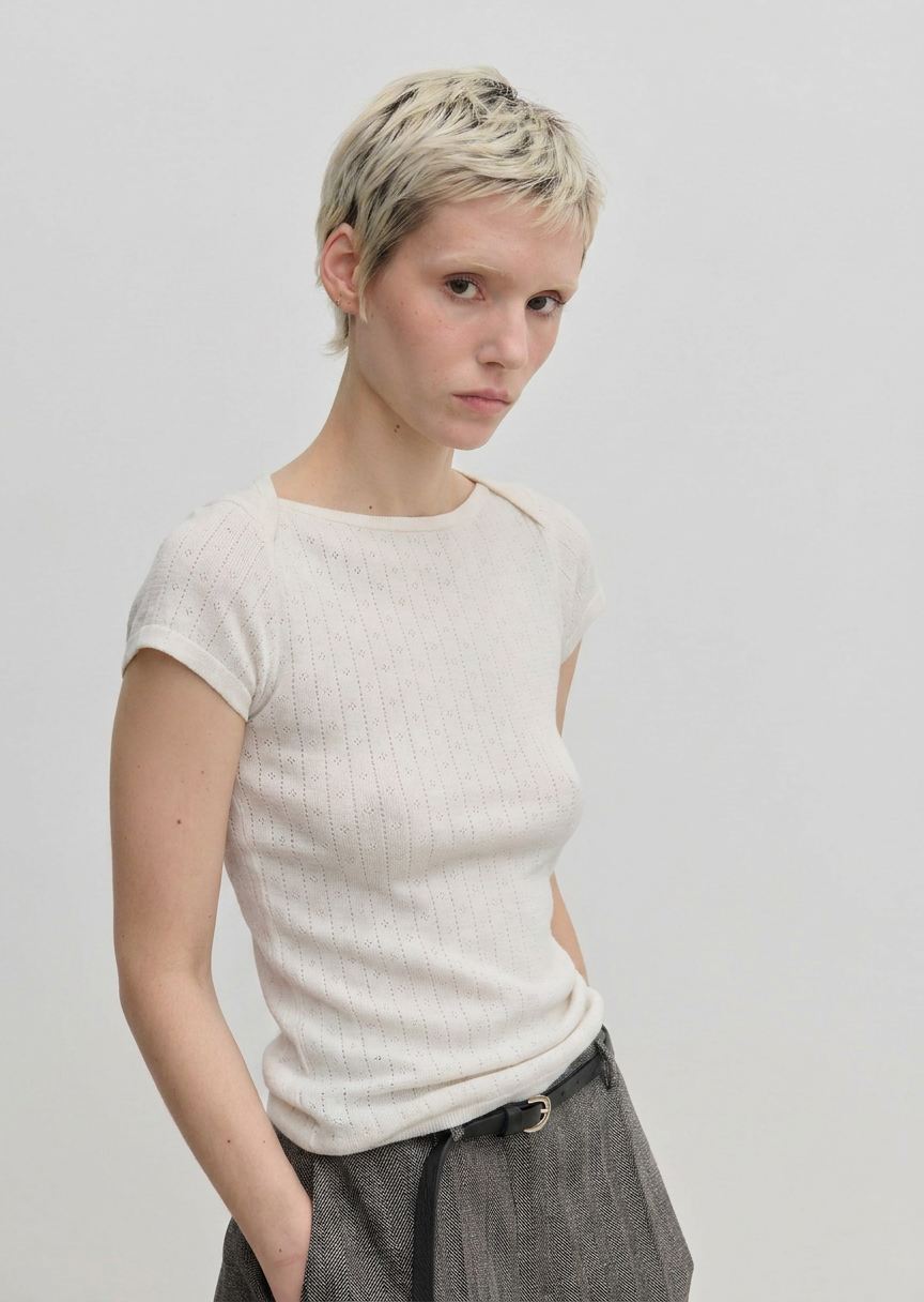 A person wearing an Erica Knit T-shirt by Herskind ApS, a slim-fit, short-sleeved, ribbed cream-colored knit t-shirt with a wide neckline.