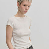 A person wearing an Erica Knit T-shirt by Herskind ApS, a slim-fit, short-sleeved, ribbed cream-colored knit t-shirt with a wide neckline.