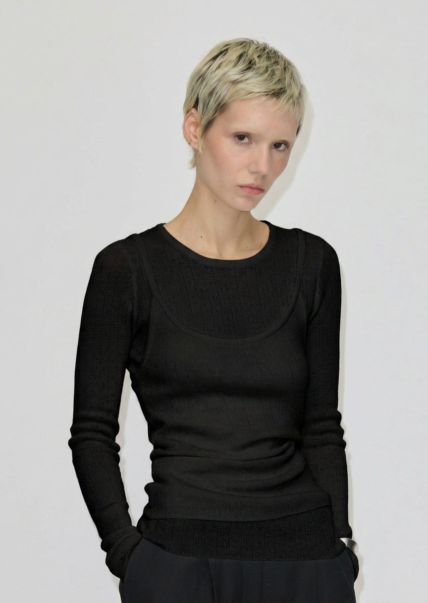 A person wearing a black, slim-fit Petit Knit Top by Herskind ApS, featuring a scoop neckline made from merino wool.