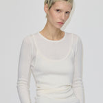 A person wears a slim-fit, cream-colored, long-sleeved, ribbed merino wool Petit Knit Top by Herskind ApS with a scoop neckline layered over a matching tank top.