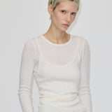 A person wears a slim-fit, cream-colored, long-sleeved, ribbed merino wool Petit Knit Top by Herskind ApS with a scoop neckline layered over a matching tank top.