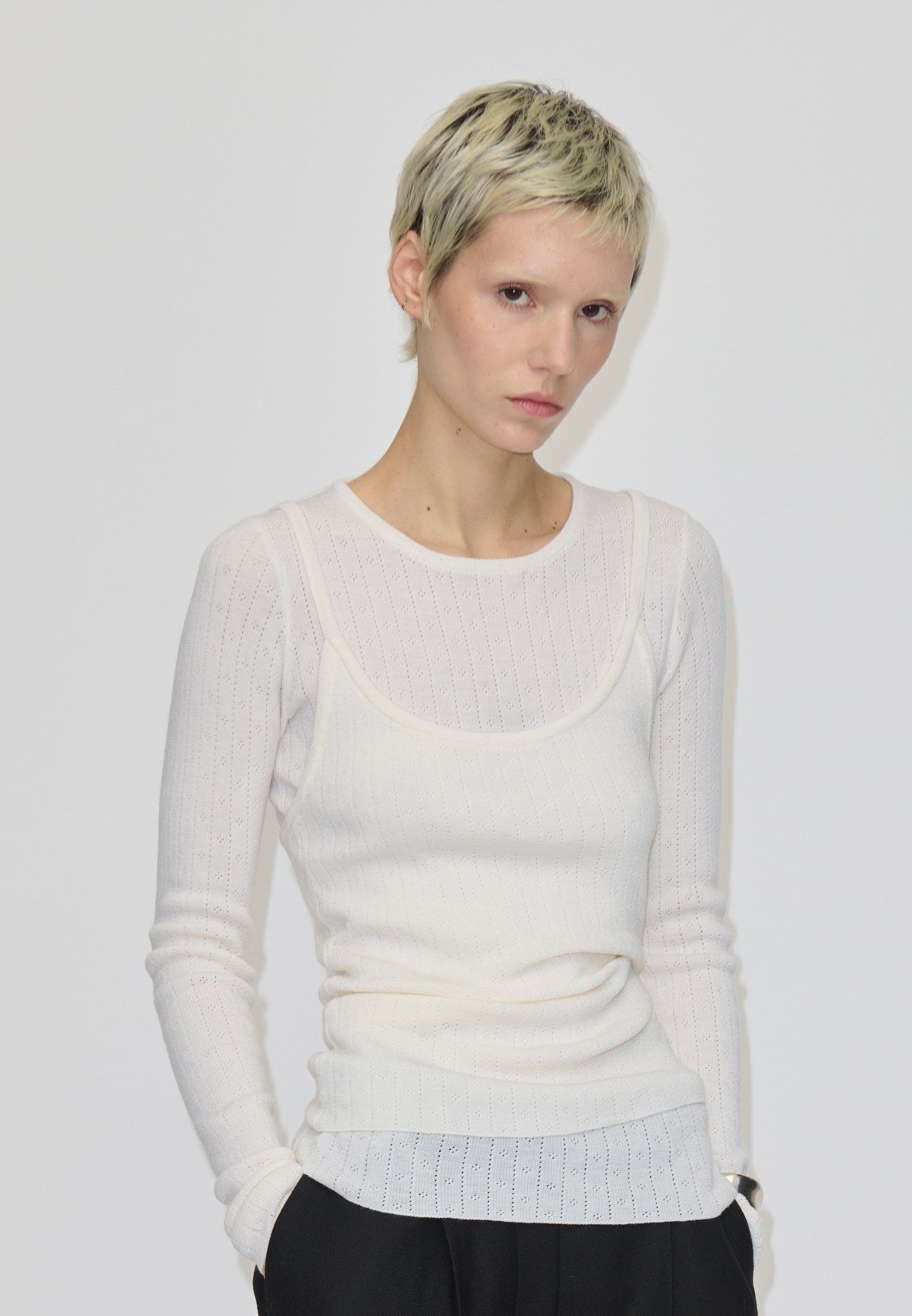 A person wears a slim-fit, cream-colored, long-sleeved, ribbed merino wool Petit Knit Top by Herskind ApS with a scoop neckline layered over a matching tank top.