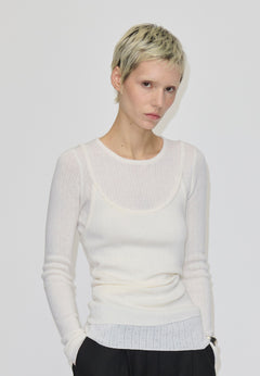 A person wears a slim-fit, cream-colored, long-sleeved, ribbed merino wool Petit Knit Top by Herskind ApS with a scoop neckline layered over a matching tank top.