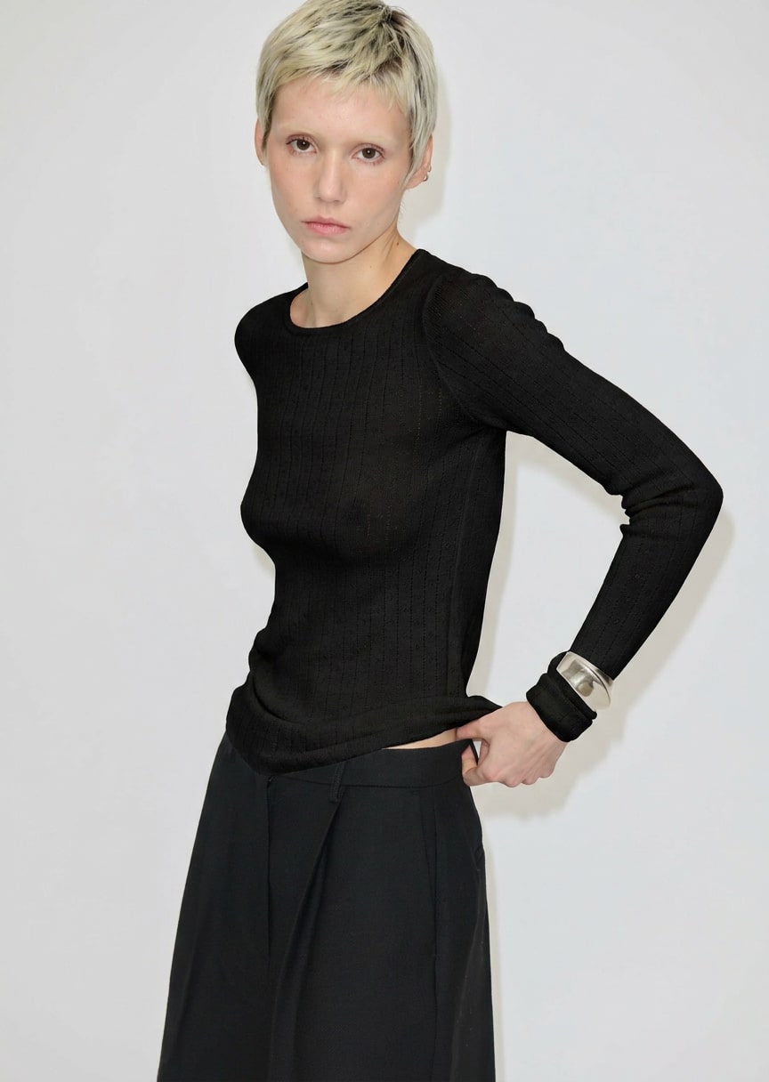 A person wears a black Camb Knit Blouse by Herskind ApS in fine-knit merino wool tucked into black trousers.