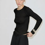 A person wears a black Camb Knit Blouse by Herskind ApS in fine-knit merino wool tucked into black trousers.