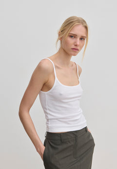 A person wearing a slim fit, white scoop-neck Poppy Top by Herskind ApS with thin straps and dark grey trousers.