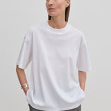 A person wears an oversized, organic cotton Herskind ApS Larsson T-shirt with a high neckline and grey patterned trousers.