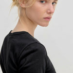 A person wearing a plain black, slim fit crew-neck River T-Shirt by Herskind ApS looks over their shoulder toward the camera.