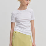 A person wearing a slim fit white River T-shirt and a pale yellow wrap skirt.