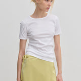 A person wearing a slim fit white River T-shirt and a pale yellow wrap skirt.