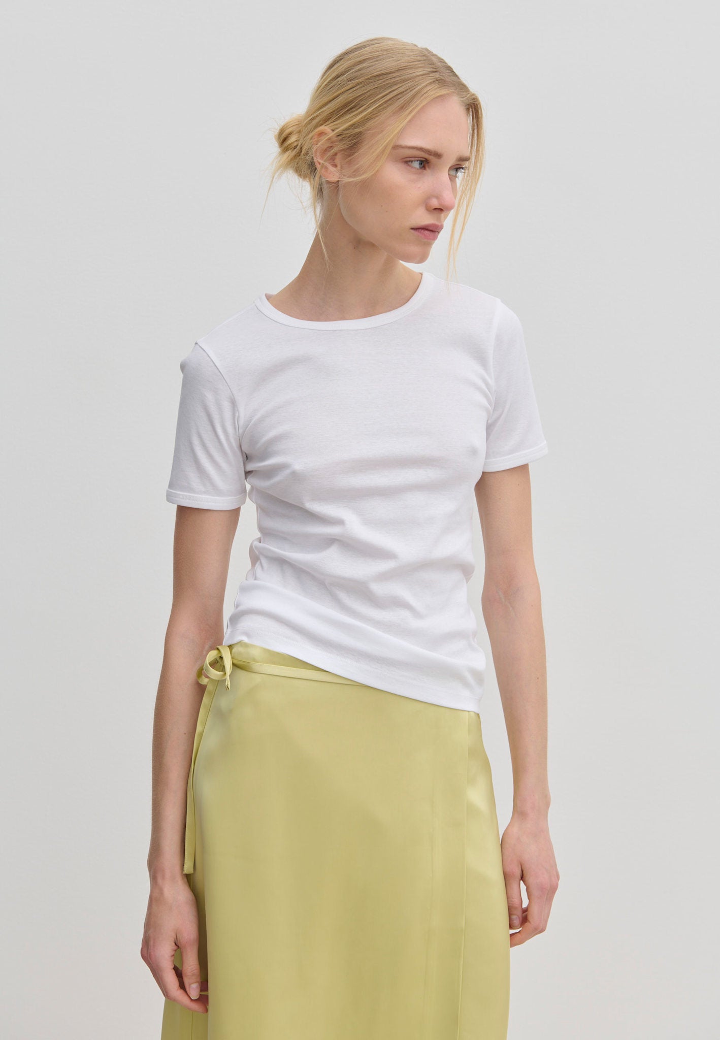 A person wearing a slim fit white River T-shirt and a pale yellow wrap skirt.