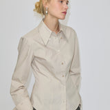 A slim fit, beige Vivienne Shirt by Herskind ApS featuring long sleeves and a pointed collar, paired with dark grey trousers.