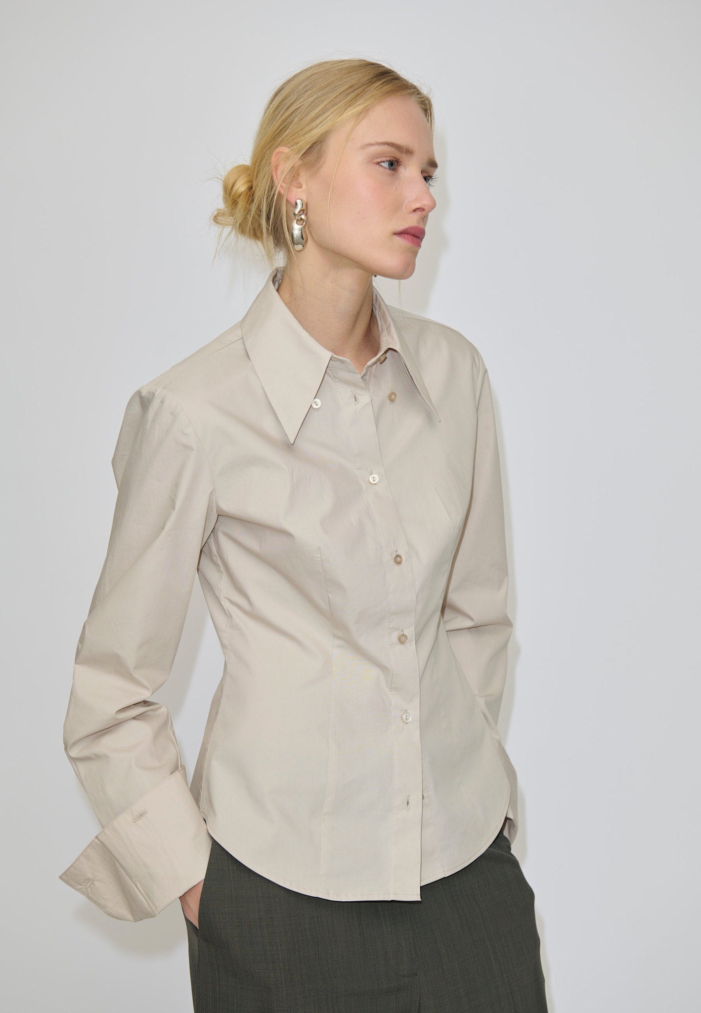 A slim fit, beige Vivienne Shirt by Herskind ApS featuring long sleeves and a pointed collar, paired with dark grey trousers.