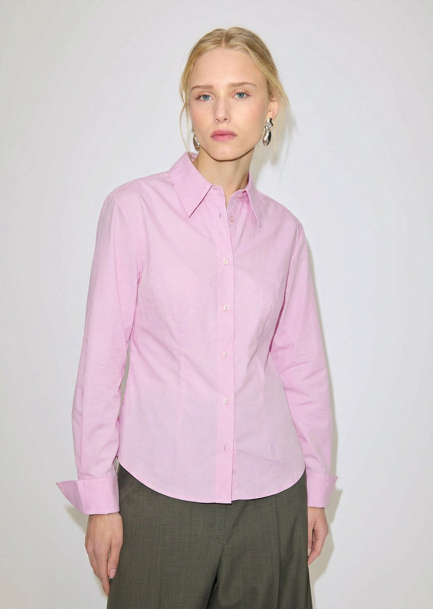 A person wears a slim fit, light pink Vivienne Shirt by Herskind ApS, made of Oeko-Tex cotton with a pointed collar and long sleeves.