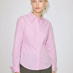 A person wears a slim fit, light pink Vivienne Shirt by Herskind ApS, made of Oeko-Tex cotton with a pointed collar and long sleeves.