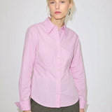 A person wears a slim fit, light pink Vivienne Shirt by Herskind ApS, made of Oeko-Tex cotton with a pointed collar and long sleeves.