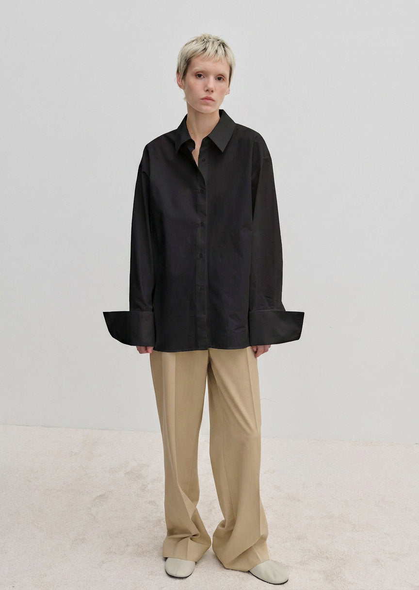 A person wearing an oversized Oeko-Tex cotton Inga Shirt by Herskind ApS with wide cuffs and tan trousers.