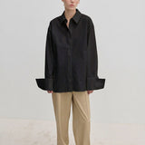 A person wearing an oversized Oeko-Tex cotton Inga Shirt by Herskind ApS with wide cuffs and tan trousers.