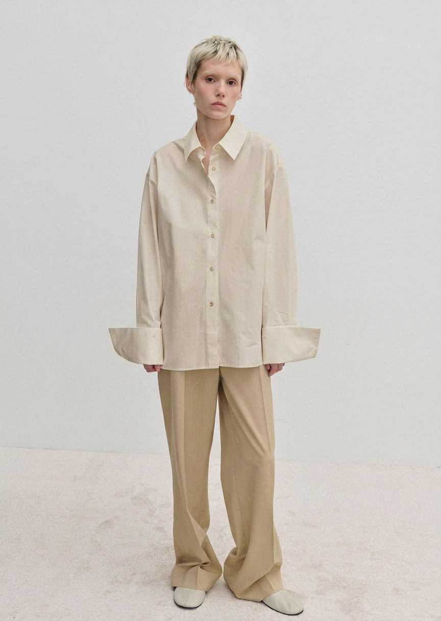 A person wearing an oversized cotton Inga Shirt by Herskind ApS with wide cuffs and matching beige trousers.