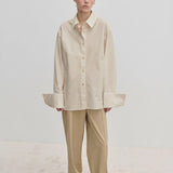 A person wearing an oversized cotton Inga Shirt by Herskind ApS with wide cuffs and matching beige trousers.