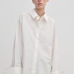 A model wears the Herskind ApS Inga Shirt, a crisp, oversized white button-down with a point collar and wide, folded cuffs.