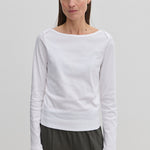 A woman wearing an Emma Blouse by Herskind ApS featuring a long-sleeved boat neckline and dark trousers.