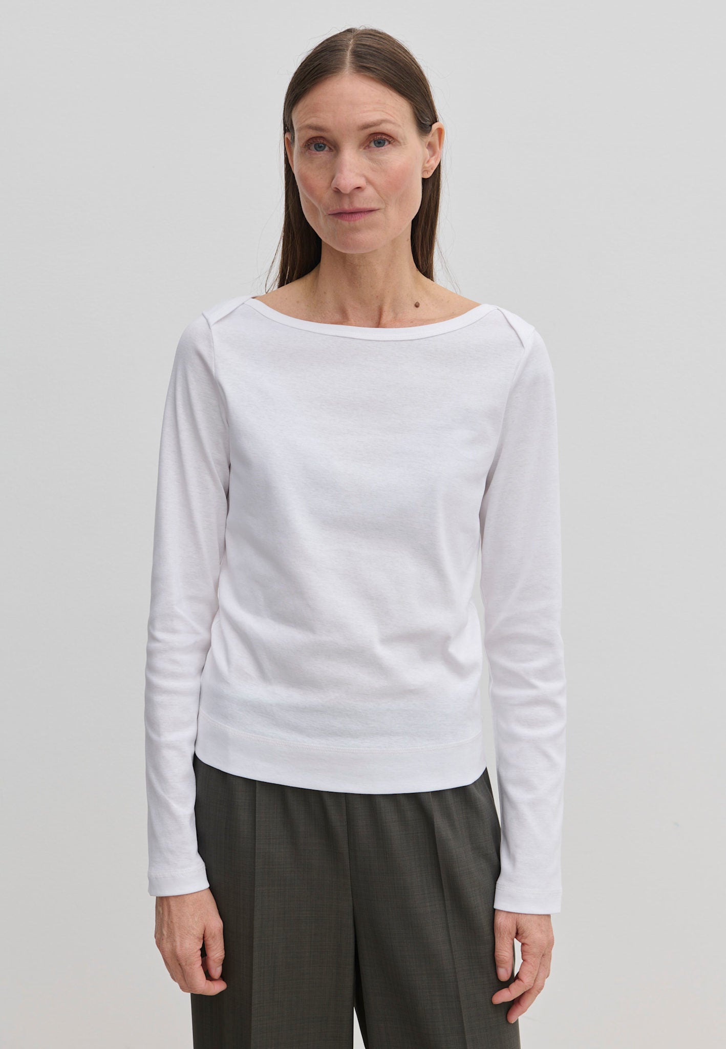 A woman wearing an Emma Blouse by Herskind ApS featuring a long-sleeved boat neckline and dark trousers.