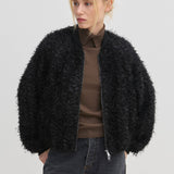 The Jimi Bomber Jacket by Herskind ApS, a black bomber jacket with balloon sleeves and a textured, fringed surface, worn over a brown collared shirt and dark grey jeans.