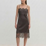 A person wears a dark midi-length Linus Dress by Herskind ApS with a lace-trimmed hem, paired with light-colored pointed-toe heels.