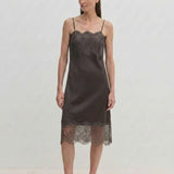 A person wears a dark midi-length Linus Dress by Herskind ApS with a lace-trimmed hem, paired with light-colored pointed-toe heels.
