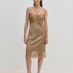 A tan midi-length Herskind ApS Linus Dress with lace-trimmed hem and neckline, worn with pointed-toe heels.