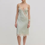 Herskind ApS Luna Dress in sage green FSC viscose, featuring delicate lace trim along the neckline, hem, and side slit of this midi slip dress.