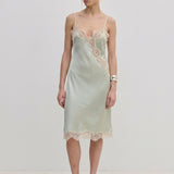 Herskind ApS Luna Dress in sage green FSC viscose, featuring delicate lace trim along the neckline, hem, and side slit of this midi slip dress.