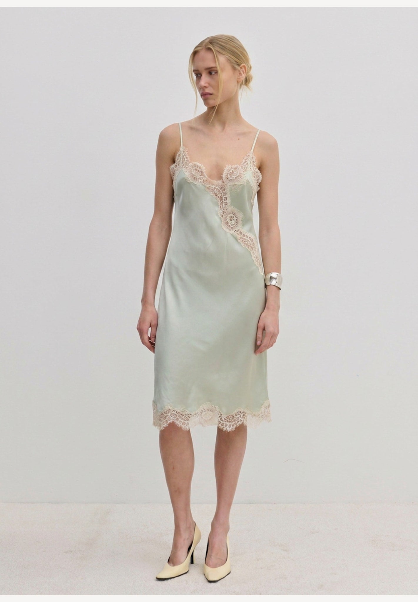 Herskind ApS Luna Dress in sage green FSC viscose, featuring delicate lace trim along the neckline, hem, and side slit of this midi slip dress.