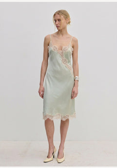 Herskind ApS Luna Dress in sage green FSC viscose, featuring delicate lace trim along the neckline, hem, and side slit of this midi slip dress.