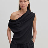 A woman wearing a black, one-shoulder Scott Top by Herskind ApS with a draped asymmetric neckline.