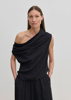 A woman wearing a black, one-shoulder Scott Top by Herskind ApS with a draped asymmetric neckline.