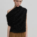 A model wears a black, textured, one-shoulder Scott Top by Herskind ApS, featuring a draped asymmetric neckline and a fringed appearance over a brown skirt.