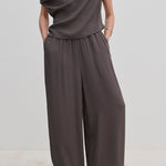 A person wears dark gray Nya Pants by Herskind ApS, featuring balloon legs, an elasticated waist, and a draped top.