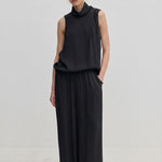 A person wearing a sleeveless black turtleneck top and matching black Nya Pants with an elasticated waist and loose-fitting, balloon leg silhouette.